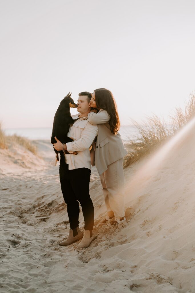Ein Hund und seine Besitzerin posieren am Strand in Holland im warmen Licht des Sonnenuntergangs.