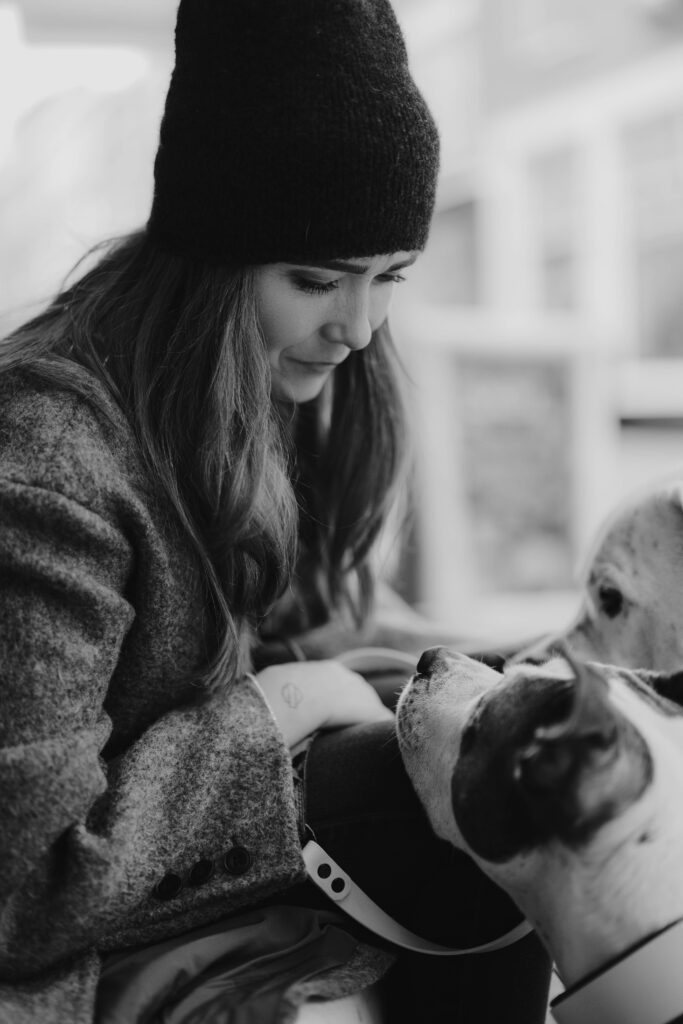 Schwarz-Weiß-Porträt: Frau mit Mütze interagiert liebevoll mit ihren Hunden bei einem Hundefotoshooting in Holland.